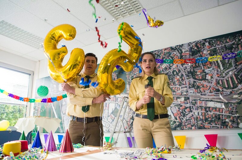 Christina (Mitsou Jung, r.) und Riedl (Paul Sedlmeir, l.) erhalten unerwarteten Besuch bei ihren Vorbereitungen zu Huberts Jubiläum. – Bild: ARD/​TMG/​Kai Neunert