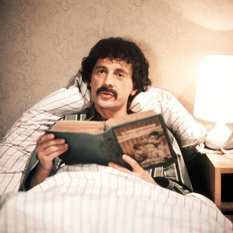 Dr. Noll (Jiri D. Novotny) liegt mit 43 Grad Fieber im Bett. Aber das macht ihm nichts, denn mit dem blauen Dampf aus der Zukunft ist er sicher, bald geheilt zu sein. Um sich die Zeit zu vertreiben, studiert er die Medizin-Bücher aus der Vergangenheit. – Bild: WDR