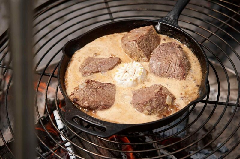 Bisonschulter in Biersoße mit geschmortem ganzen Knoblauch köchelt in der Pfanne auf dem Grill. – Bild: Marian Mok /​ BR, Yalla Productions GmbH /​ BR/​Yalla Productions GmbH/​Marian Mok