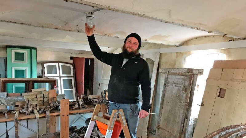 Elektriker Nikolas Aschinger beim Reparieren einer Lampe in einem ehemaligen Schweinestall um 1800. – Bild: NDR/​Doclights GmbH/​Jela Henning