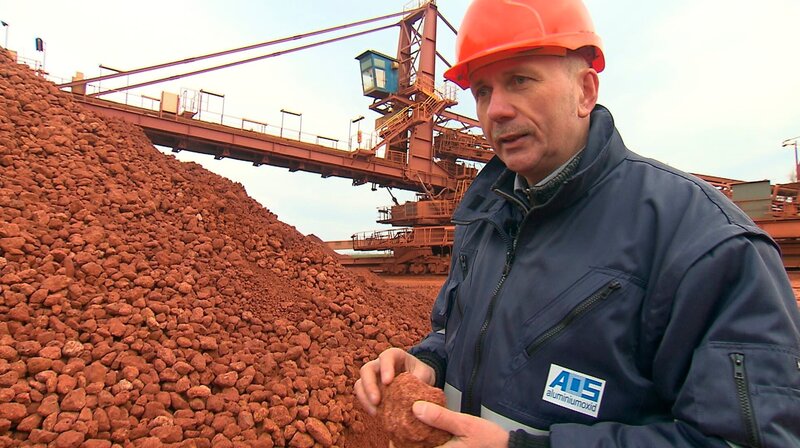 Bauxidhalde in Stade: Aus der roten Erde wird bei der AOS Aluminiumoxid gewonnen, ein feines weißes Pulver. – Bild: NDR/​FILMBLICK Hannover