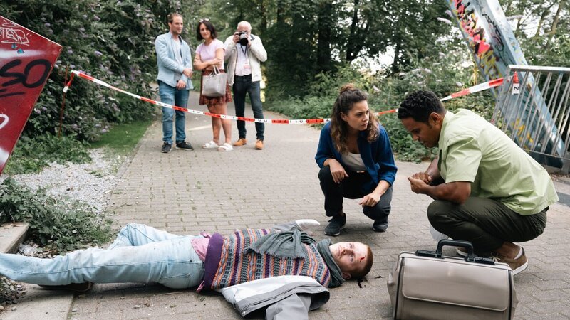 Dr. Adam Makena (Stephen Appleton, r.) berichtet Lilly Funke (Tatjana Kästel, 2.v.r.), dass der Tote infolge eines stumpfen Schädeltraumas starb. Die Hauptkommissarin erkennt in dem jungen Mann Marten Keller (Cedric Sprick-Benz), den Sprecher einer bekannten Klimaaktivistengruppe. – Bild: ZDF