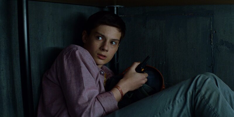 Louis (Oliver Cunliffe) ist in den Raum im Keller der verlassen wirkenden Hütte geschlichen. Als er sich dort heimlich umschaut, hört er Geräusche und versteckt sich unter dem Schreibtisch. – Bild: ZDF/​Zodiak Kids Studio UK Limited