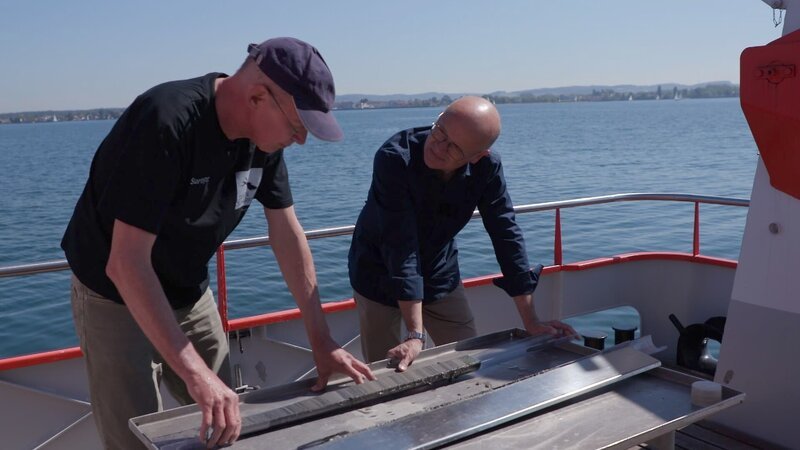 Dr. Martin Wessels (links) vom Institut für Seenforschung in Langenargen zeigt Karsten Schwanke einen Sedimentbohrkern vom Grund des Bodensees aus 160 Metern Tiefe. Damit rekonstruiert der Forscher die Geschichte des Sees. – Bild: Klaus Hernitschek /​ BR /​ BR/​Klaus Hernitschek