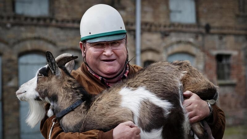 Krause (Horst Krause) hebt die Ziege Rosi aus dem Beiwagen seines Motorrades. – Bild: rbb/​Arnim Thomaß