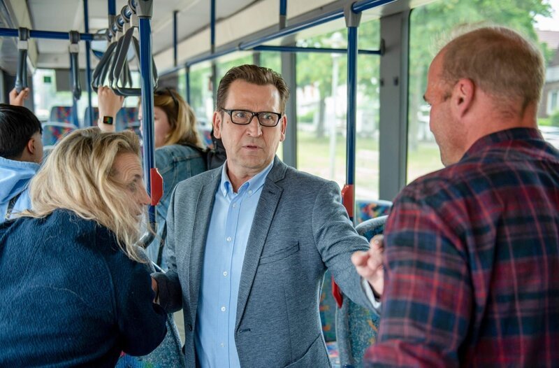 Lars Englen (Ingo Naujoks, M.) hat Mühe, im fahrenden Bus für Ruhe und Ordnung zu sorgen (mit Kompars:innen). – Bild: ORF/​ONE GATE/​ARD/​Thorsten Jander