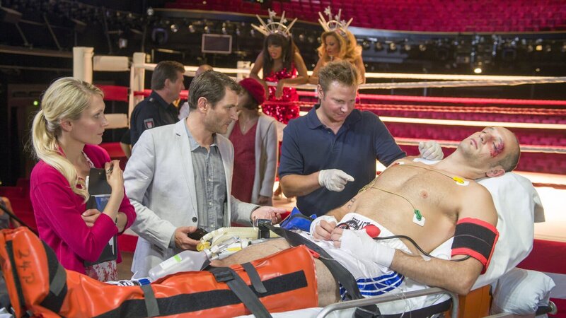 Drew Sarich (Drew Sarich, r.) der Hauptdarsteller des Musicals „Rocky“ ist nach einer Vorstellung hinter der Bühne zusammengebrochen. Haase (Fabian Harloff, 2.v.r.) kümmert sich um seinen Patienten und lässt den künstlerischen Leiter Mikkelsen (Alex Brendemühl, 2.v.l.) und dessen Assistentin Janne (Mareile Moeller) gleich wissen, dass sie mit Drew für die Abendvorstellung nicht mehr rechnen können. – Bild: ZDF