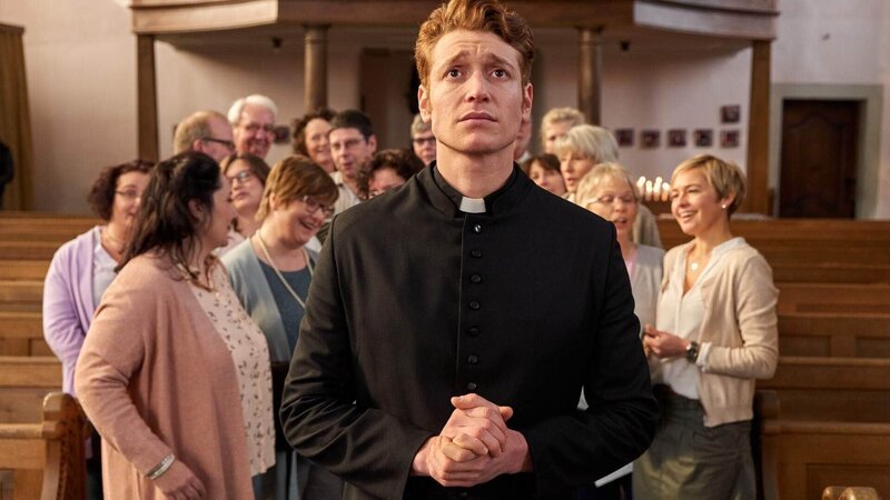 Maik (Daniel Donskoy) wird überschwenglich vom Kirchen-Chor begrüßt. Ihn beschleicht ein mulmiges Gefühl. – Bild: TVNOW /​ Frank Dicks