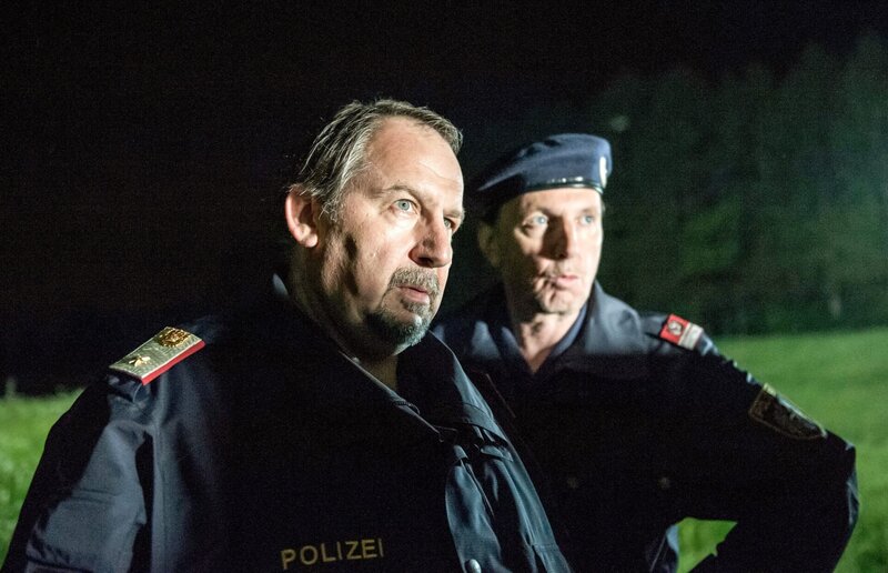 Felix Hörtnagel (Wolf Bachofner, l.), Polizeichef von Mairach, wünscht die SOKO Kitzbühel zum Teufel, die sich in die inneren Angelegenheiten seines Reviers einmischt, um einen Mord aufzuklären. Sein Mitarbeiter Josef Schratt (Rainer Egger, r.) ist auf seiner Seite. – Bild: ORF/​BEO-Film/​Stefanie Leo