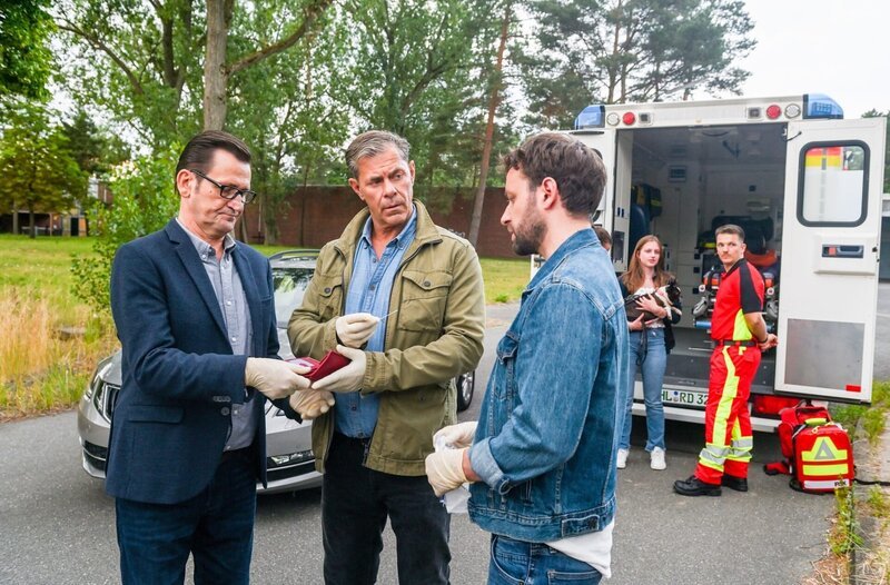 Am Tatort zeigen sich die beiden Ermittler Lars Englen (Ingo Naujoks, l.) und Finn Kiesewetter (Sven Martinek, 2.v.l.) sichtlich betroffen. Sie blicken zu Gregor (Jonas Minthe, r.), der ihnen ebenfalls bestürzt, das Alter des Mordopfers mitteilt. – Bild: ORF/​ONE GATE/​ARD/​Nicole Manthey