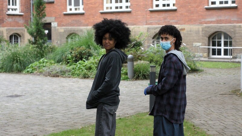 Bei einem Spaziergang über den Klinikhof machen Ronnie (Zoe Magdalena, l.) und Milan (Amadin Piatello, r.) eine interessante Beobachtung: Ist das nicht der von Kimmi gefeierte Social-Media-Star 365Tom da hinten in den Büschen? Laut Social-Media-Profil sollte er eigentlich auf Bali sein. – Bild: ZDF