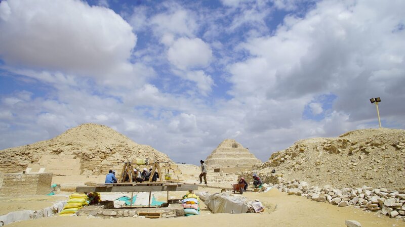 Saqqara, Ägypten – Die Mumienwerkstatt und der Gemeinschaftsgrabschacht liegen im Schatten von zwei der berühmtesten Pyramiden von Saqqara – der Stufenpyramide und der Unas-Pyramide. Arbeiter nähern sich der Winde, mit der unschätzbare Artefakte aus dem Grabschacht befördert werden. – Bild: National Geographic/​Rafael Libson-Hochenberg