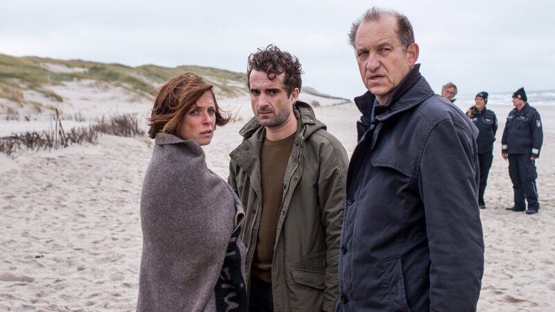 Hinnerk Feldmann (Oliver Wnuk, M.) und Carl Sievers (Peter Heinrich Brix, r.) müssen Ina Behrendsen (Julia Brendler, l.) beistehen, die gerade ihren Freund, den Robbenschützer Leo Fischer, tot am Strand gefunden hat. – Bild: ZDF