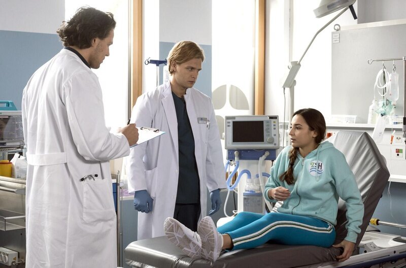 Die Schwimmlehrerin Kaja Badlin (Rona Özkan, r.) wird von Dr. Noah Mattes (Christian Martin Schäfer, l.) sowie Mikko (Luan Gummich, M.) im Klinikum aufgenommen und untersucht. Sie gibt an, im Schwimmbad ausgerutscht zu sein. – Bild: ARD