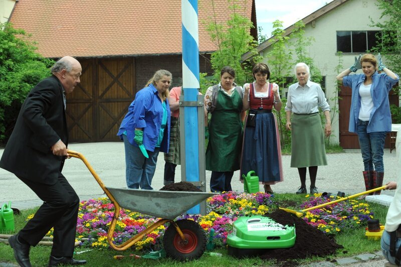 Pfarrer Kurz versucht den automatischen Rasenmäher zu stoppen. Von links: Pfarrer Kurz (Hans Stadlbauer), Monika Vogl (Christine Reimer), Rosi Brunner (Brigitte Walbrun), Theresa Brunner (Ursula Erber) und Uschi Guggenmoser (Silke Popp). – Bild: BR/​Marco Orlando Pichler