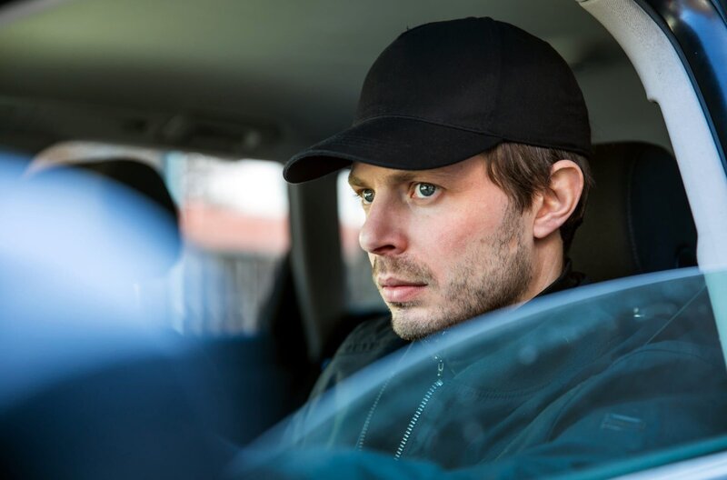 Frederick Becker beobachtet vom Auto aus die Praxis, in der sich seine Frau untersuchen lässt. – Bild: ARD/​TMG/​Chris Hirschhäuser