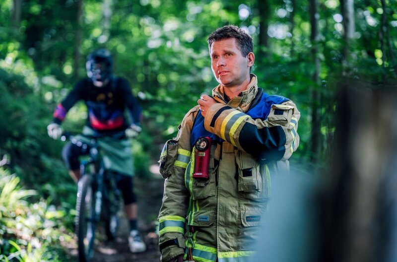 Ein Berufsfeuerwehrmann alarmiert das Mehrzweckfahrzeug (MTZ) zur Rettung eines gestürzten Downhill-Bikers. – Bild: SWR/​Sebastian Drolshagen