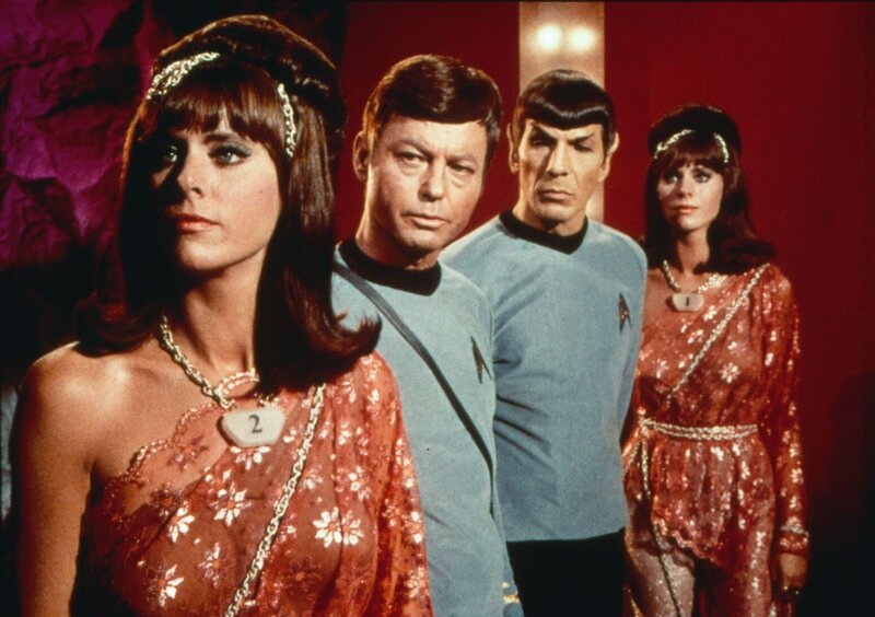 Dr. McCoy (DeForest Kelley, 2.v.l.) und Mr. Spock (Leonard Nimoy, 2.v.r.) beobachten leicht abgestoßen die fremde Welt von Harry Mudd. Der Herrscher hat sich eine Bevölkerung aus Androiden geschaffen, über die er verfügen kann. Die Roboter-Frauen (Darstellerinnen unbekannt) gleichen einander wie ein Ei dem anderen. – Bild: Tele 5