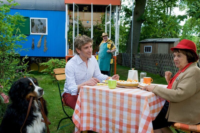Fritz (Guido Hammesfahr, l.) mit seiner Oma Ilse (Us Conradi, r.). Sie ist von Bauwagen, Keks und Kuchen sowie dem Nachbarn (Helmut Krauss, l.) als Hausgärtner begeistert. – Bild: Antje Dittmann /​ ZDF und Antje Dittmann