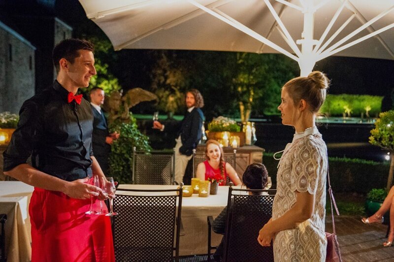 Während Alexander (Frederik Götz, 3.v.l.) sich mit einem der Gäste unterhält, läuft Josefin (Sina Zadra, r.) an ihm vorbei. Er erkennt sie von ihrer Begegnung am Flughafen wieder. – Bild: TVNOW