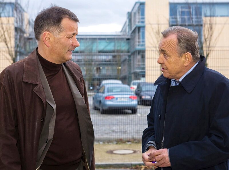 Prof. Simoni (Dieter Bellmann, re.) will in der Klinik nach dem Rechten schauen. Als er vor der Klinik auf Dr. Heilmann (Thomas Rühmann, li.) trifft, erfährt er, dass gerade eine Art prominenter Patient in der Klinik weilt, der auf einen OP-Fehler Brentanos pocht. – Bild: MDR/​Krajewsky
