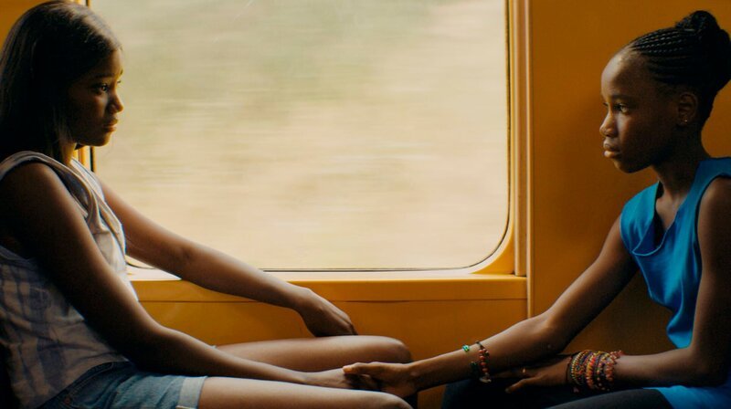 Marieme (l, Karidja Touré) und ihre Schwester Bébé (Simina Soumaré) fahren mit dem Zug nach Hause. – Bild: WDR/​Alamode Film