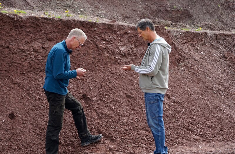 Der Erfinder Axel Lange (rechts) und Produktionsleiter Iko Alten in der Tongrube. Sie untersuchen die verschiedenen Tonschichten, aus dem Lehmplatten für die Raumkühlung hergestellt werden. – Bild: MDR/​Jette Berger
