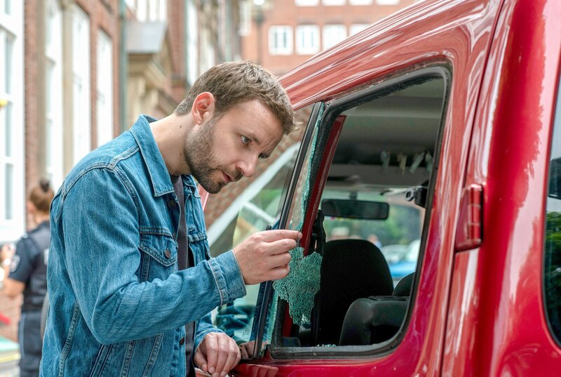 Gregor (Jonas Minthe) untersucht die zerstörte Fensterscheibe am Auto des Mordopfers. – Bild: ORF/​ONE GATE/​ARD/​Thorsten Jander