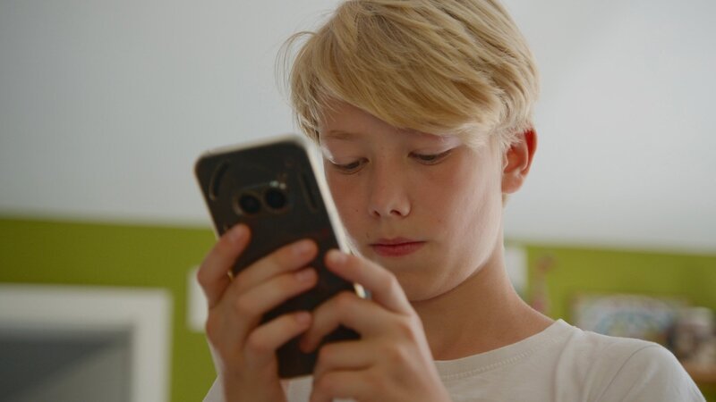 NZZ Format Aufwachsen ohne Smartphone – Ist eine Kindheit ohne Tiktok und Co. möglich? John mit Smartphone – Bild: SRF/​NZZ Format