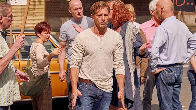 Stefan Vollmer (Hendrik Duryn, M.) trifft auf die wütende Menge, die gegen den verurteilten Triebtäter demonstriert, der in die Nähe der Schule gezogen ist. – Bild: TVNOW /​ Frank Dicks