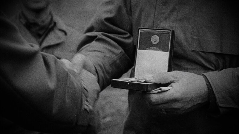Ein Mann überreicht einer anderen Person eine Medaille und schüttelt ihr zur Gratulation die Hand. – Bild: History