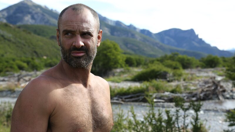 Ed Stafford standing by a body of water in Patagonia in a mountainous region. – Bild: Discovery Communications