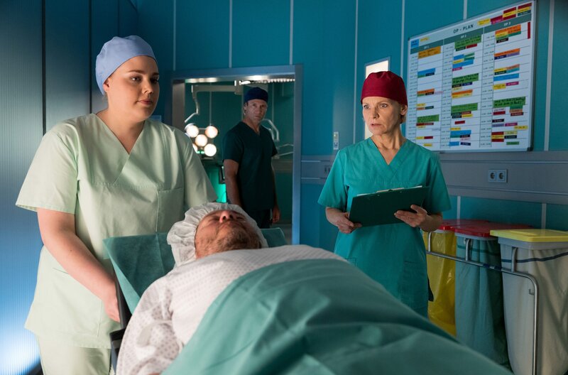 Dr. Kathrin Globisch (Andrea Kathrin Loewig, re.) traut ihren Augen nicht, als Schwester Miriam (Christina Petersen, li.) Michael Linse (Tom Jahn, mi.) an ihr vorbeischiebt. Genau diese Begegnung wollte Dr. Martin Stein (Bernhard Bettermann, hi.) eigentlich verhindern. – Bild: MDR/​Saxonia Media/​Rudolf Wernicke