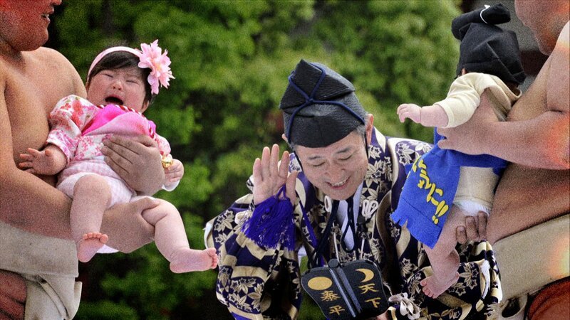 Zwei Männer halten Babys in ihren Armen, während ein Richter in traditioneller Kleidung zuhört, welches Baby am lautesten weint. – Bild: History