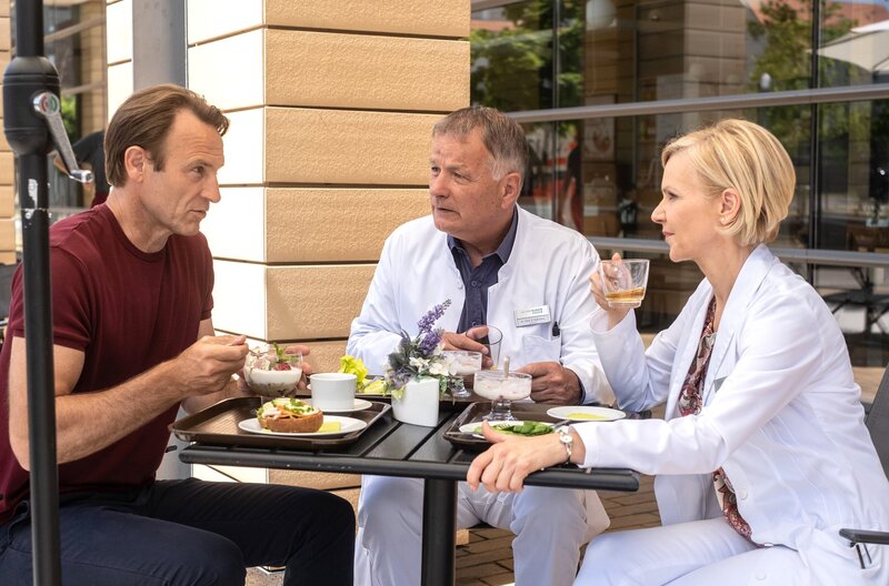 Dr. Martin Stein (Bernhard Bettermann, li.) ist seit langem mal wieder ausgeschlafen, da sein Freund und Kollege Dr. Roland Heilmann (Thomas Rühmann, mi.) in der Nacht auf Martins Enkelin aufgepasst hat. Zu Martins Überraschung bietet Roland sich sofort wieder an. Dr. Kathrin Globisch (Andrea Kathrin Loewig, re.) ahnt den wahren Grund für Rolands Verhalten. – Bild: Robert Strehler