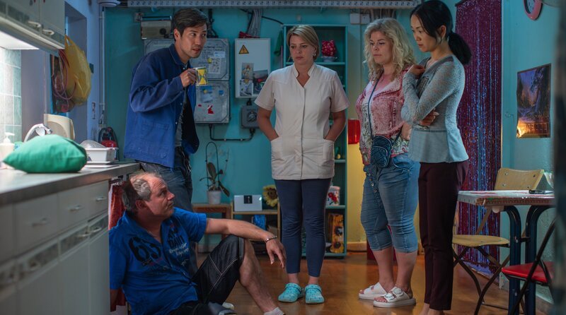 Schlechte Nachrichten für den Salon: Mario (Jörg Malchow) unterrichtet das versammelte Team über den Wasserschaden. V. li. n. re.: Fritz (Paul Jumin Hoffmann), Kathi (Jördis Triebel), Nadja (Marie Schöneburg) und Jenny (Yvonne Yung Hee Bormann). – Bild: ARD Degeto Fim/​UFA Fiction GmbH/​Oliver Vaccaro