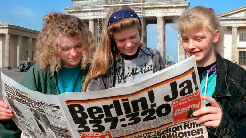 Am Brandenburger Tor in Berlin informieren sich Jugendliche am 23. Juni, einen Tag nach der Abstimmung im Deutschen Bundestag über den Regierungssitz, in einer Zeitung. – Bild: WDR/​picture-alliance/​dpa