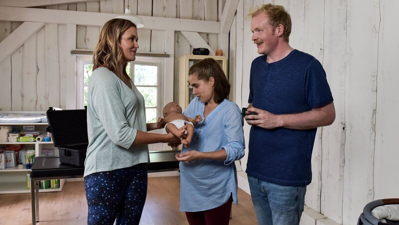 Lena Lorenz (Judith Hoersch, l.) erklärt den werdenden Eltern Alina Moosleitner (Anne-Marie Lux) und Tim Scheuer (Sebastian Griegel), wie der Babysimulator funktioniert und worauf sie achten müssen. – Bild: ZDF