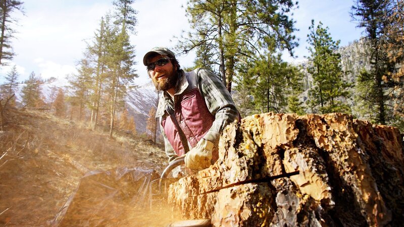 Wes Gregory sawing down a tree, smiling. – Bild: Warner Bros. Discovery Wes Gregory sawing down a tree, smiling. – Bild: Warner Bros. Discovery