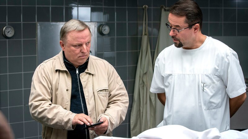 Auf dem Handy von Prof. Karl-Friedrich Boerne (Jan Josef Liefers, r) schaut sich Frank Thiel (Axel Prahl, l) an, welche Bilder gerade im Internet kursieren: Er wurde fotografiert, wie er scheinbar lachend am Tatort steht. – Bild: WDR/​Thomas Kost