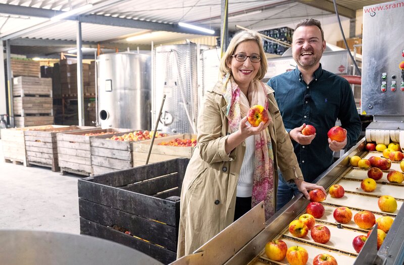 Yvonne Willicks (l) darf heute ordentlich mit anpacken. Am Sortierband von Fruchtsaftproduzent Florian Milke (r) darf Deutschlands bekannteste Hauswirtschaftsmeisterin mitsortieren. Nur die schönsten landen später im Apfelsaft. – Bild: WDR/​Melanie Grande