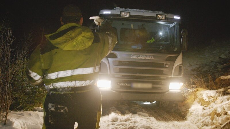 Mit Thord am Steuer führt Terje ihn, während er einen Müllwagen rückwärts einen schmalen Hügel hinauffährt. – Bild: National Geographic for Disney /​ Disney