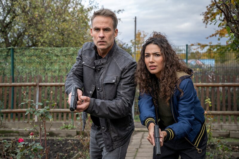 Als Jan Maybach (Marco Girnth, l.) und Kim Nowak (Amy Mußul, r.) einen weiteren Klienten des Gerichtsvollziehers befragen wollen, wird plötzlich aus der Gartenlaube geschossen. – Bild: Uwe Frauendorf /​ ZDF Enterprises GmbH