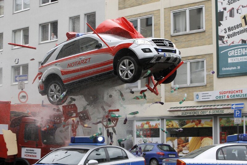 Semir durchbricht mit einem gekaperten Notarztwagen eine Polizeiabsperrung und fliegt über die Kreuzung … – Bild: RTL Crime /​ Guido Engels