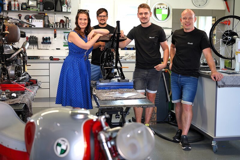 Die Puch Motorrad-Sammler Raphael Neumann, Manuel Schuster, Christian Galli (von links) mit Moderatorin Conny Bürgler (ganz links) in der Werkstatt, aufgenommen während ServusTV's "Heimatleuchten" in Aigen, St. Martin im Sulmtal. – Bild: ServusTV /​ Degn Film /​ Brigitte Erhart