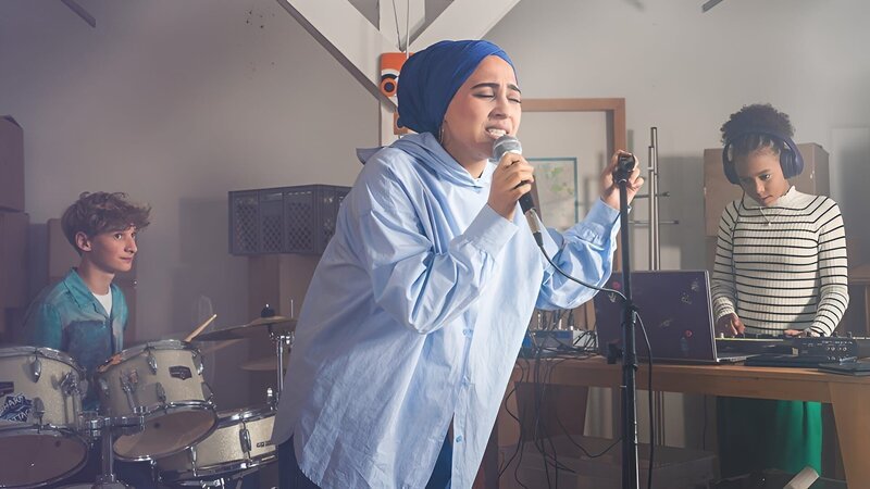 Frau Amani (Tua El-Fawwal, Mitte) performt zum Song von Mikka (Jona Kirchner, links) und Ruby (Sonia Kantati, rechts). – Bild: mdr/​Saxonia Media/​Thomas Dietze