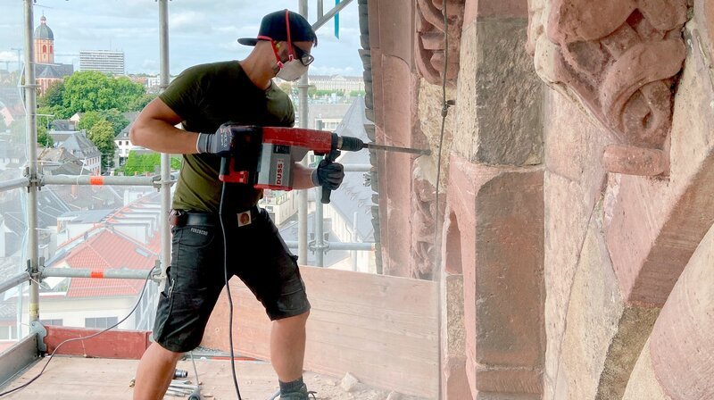 Am Südgiebel des Querhauses stemmt Steinmetz Manuel Heininger ein Stück beschädigten Sandstein aus der Wand, da es ersetzt werden muss. – Bild: SWR, honorarfrei – Verwendung gemäß der AGB im engen inhaltlichen, redaktionellen Zusammenhang mit genannter SWR-Sendung bei Nennung „Bild: SWR“ (S2+). SWR Presse/​Bildkommunikation, Baden-Baden, Tel: 07221/​929⁠–⁠26868, foto@swr.de