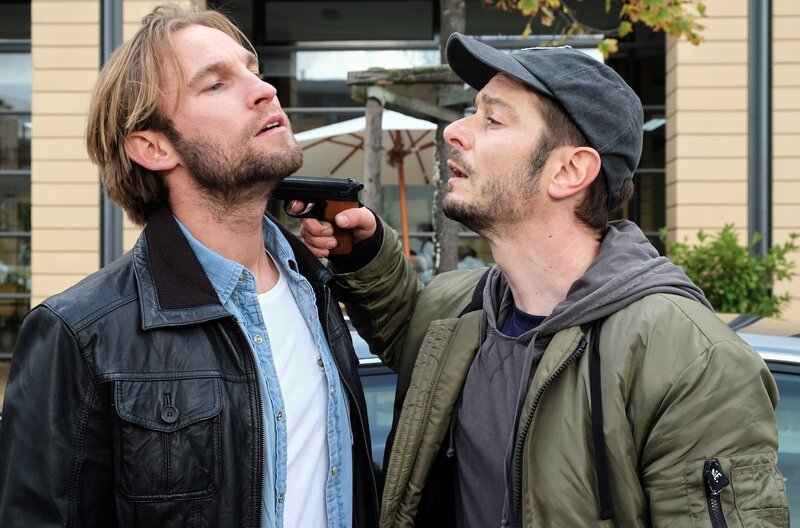 Während Felix Sonntag (Jochen Matschke, li.) vor der Sachsenklinik auf seine Freundin Sarah Marquardt wartet, steht plötzlich ein alter Bekannter vor ihm. Max Hellmann (Michael Baral, re.) hatte vor einigen Wochen das Computersystem der Klinik lahmgelegt und somit viele Menschenleben gefährdet. Dafür wurde er nun zu zwei Jahren Haft und Schadenersatz verurteilt. Max macht Felix dafür verantwortlich und fordert nun bewaffnet eine Geld-Transaktion auf sein Konto von ihm. – Bild: BR/​MDR/​Saxonia Media Filmproduktions GmbH/​Sebastian Kiss