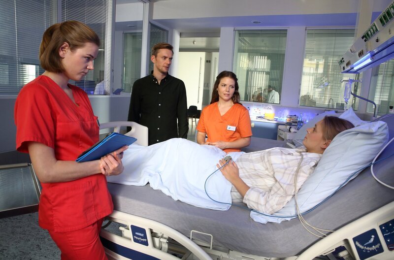 Louisa (Llewellyn Reichman, l.) und Maxi (Leonie Rainer, 3.v.l.) kümmern sich um Tina Fischer (Charlotte Puder, liegend), die gerade eine komplizierte Entbindung hinter sich hat. Ihr Mann Karsten (Jan Dose, 2.v.l.)  ist besorgt. – Bild: ARD/​Uwe Köhn