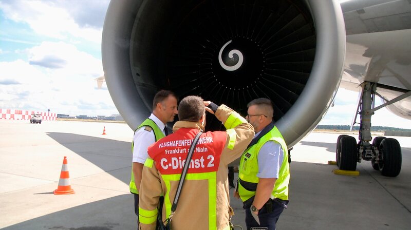 Ein Frachtflieger hebt ab, plötzlich kreuzt ein Vogelschwarm die Startbahn. Mehrere Tauben werden von den Triebwerken angesaugt. Ein Triebwerk hat was abbekommen. Der Pilot (li.) begutachtet mit einem Feuerwehrmann und einem Maintenance-Mitarbeiter das beschädigte Triebwerk. – Bild: HR